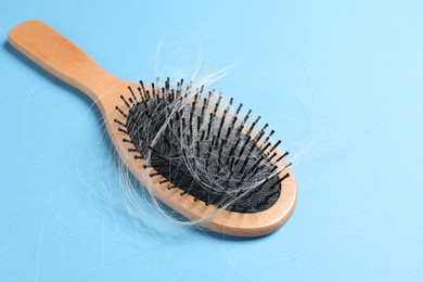 Photo of Wooden brush with lost hair on light blue background