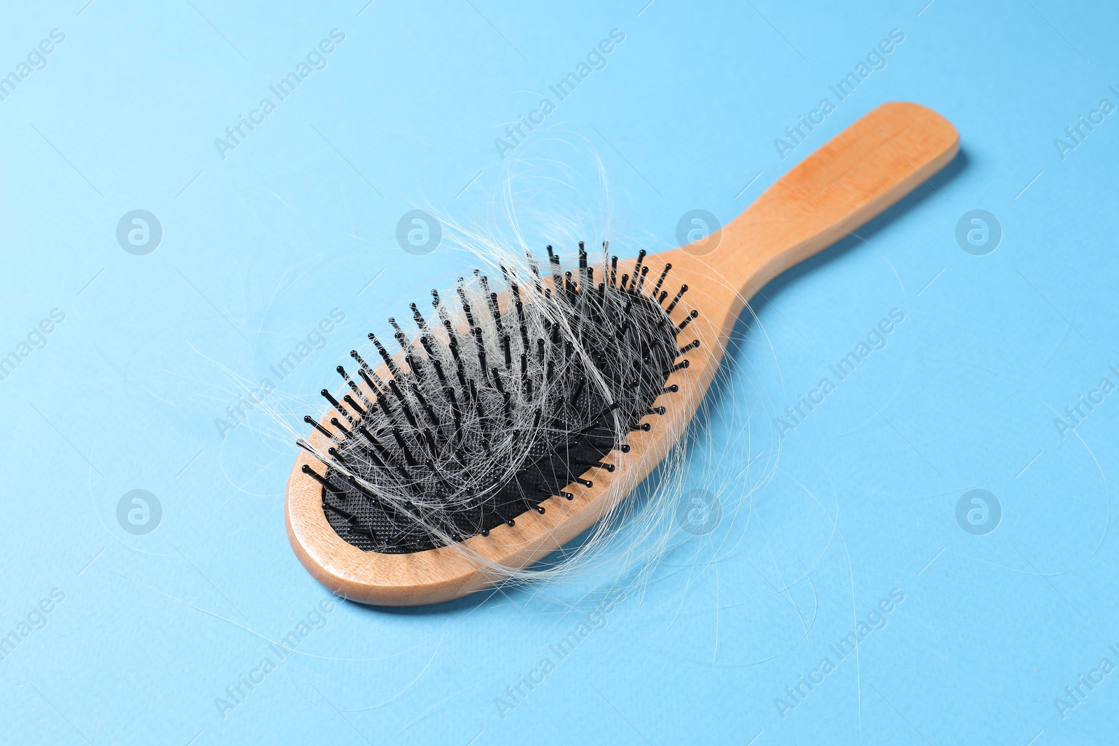 Photo of Wooden brush with lost hair on light blue background