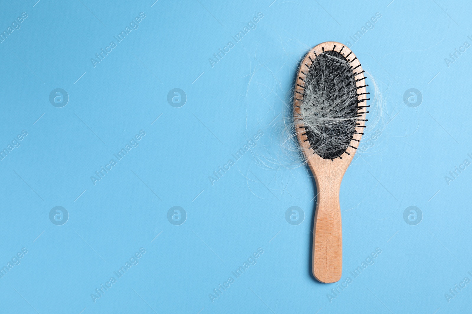 Photo of Wooden brush with lost hair on light blue background, top view. Space for text