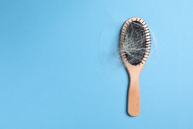 Photo of Wooden brush with lost hair on light blue background, top view. Space for text