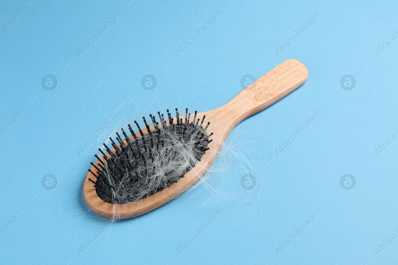 Photo of Wooden brush with lost hair on light blue background