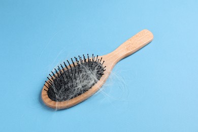 Photo of Wooden brush with lost hair on light blue background