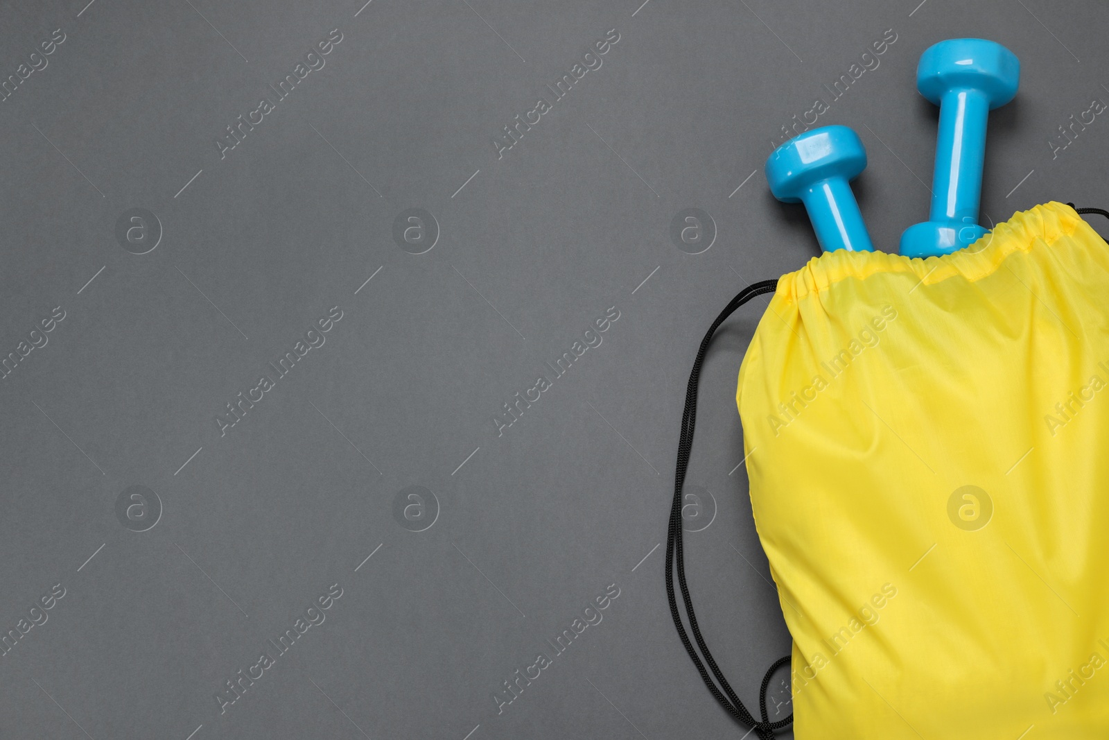 Photo of Yellow drawstring bag and dumbbells on grey background, top view. Space for text