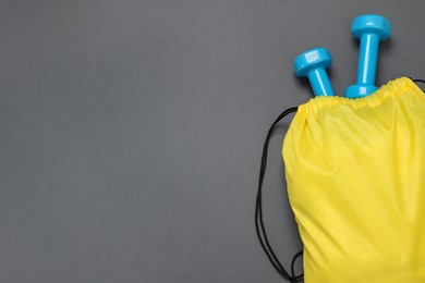 Photo of Yellow drawstring bag and dumbbells on grey background, top view. Space for text