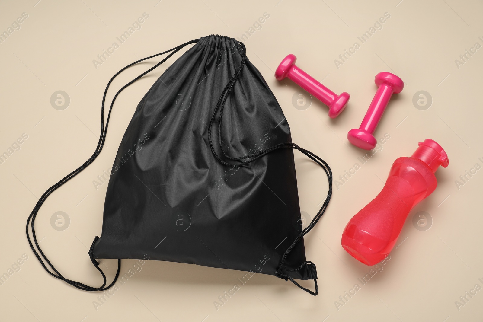 Photo of Black drawstring bag, bottle and dumbbells on beige background, flat lay