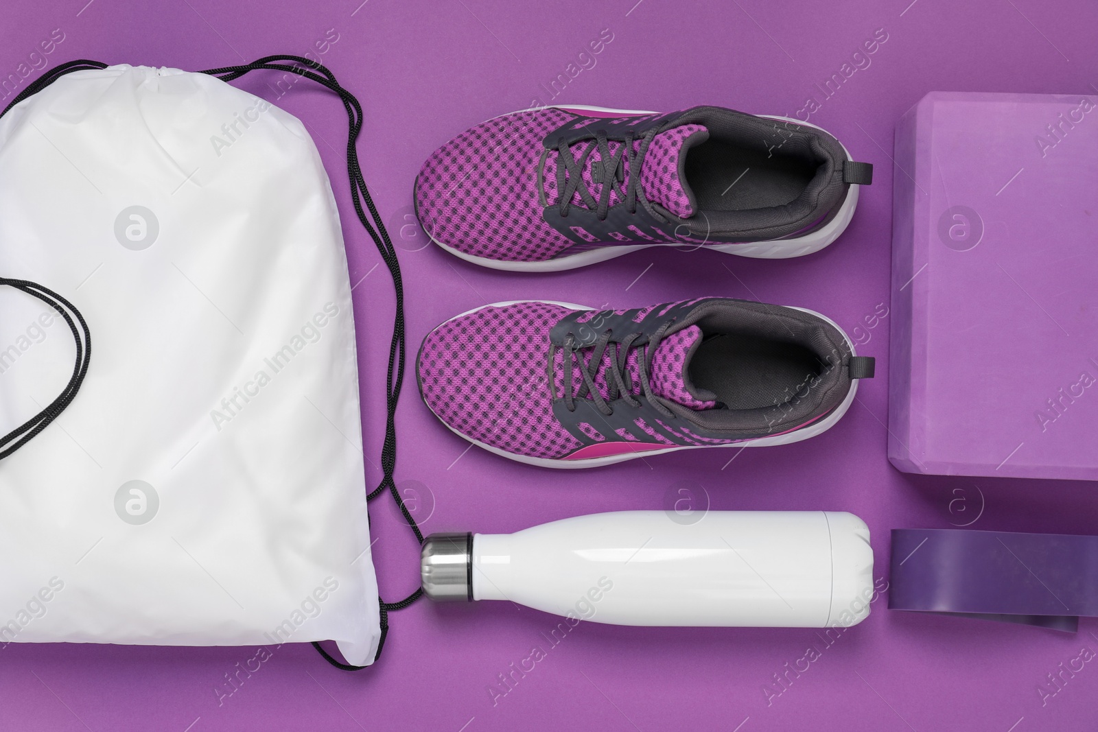 Photo of White drawstring bag, thermo bottle, sneakers and yoga block on purple background, flat lay