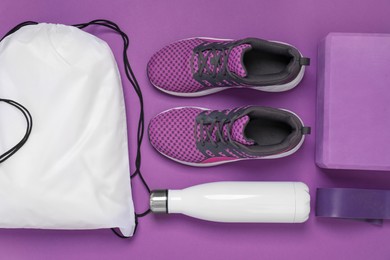 White drawstring bag, thermo bottle, sneakers and yoga block on purple background, flat lay