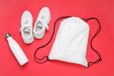 White drawstring bag, thermo bottle and sneakers on red background, flat lay