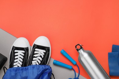 Blue drawstring bag, thermo bottle, skipping rope and sneakers on red background, flat lay. Space for text