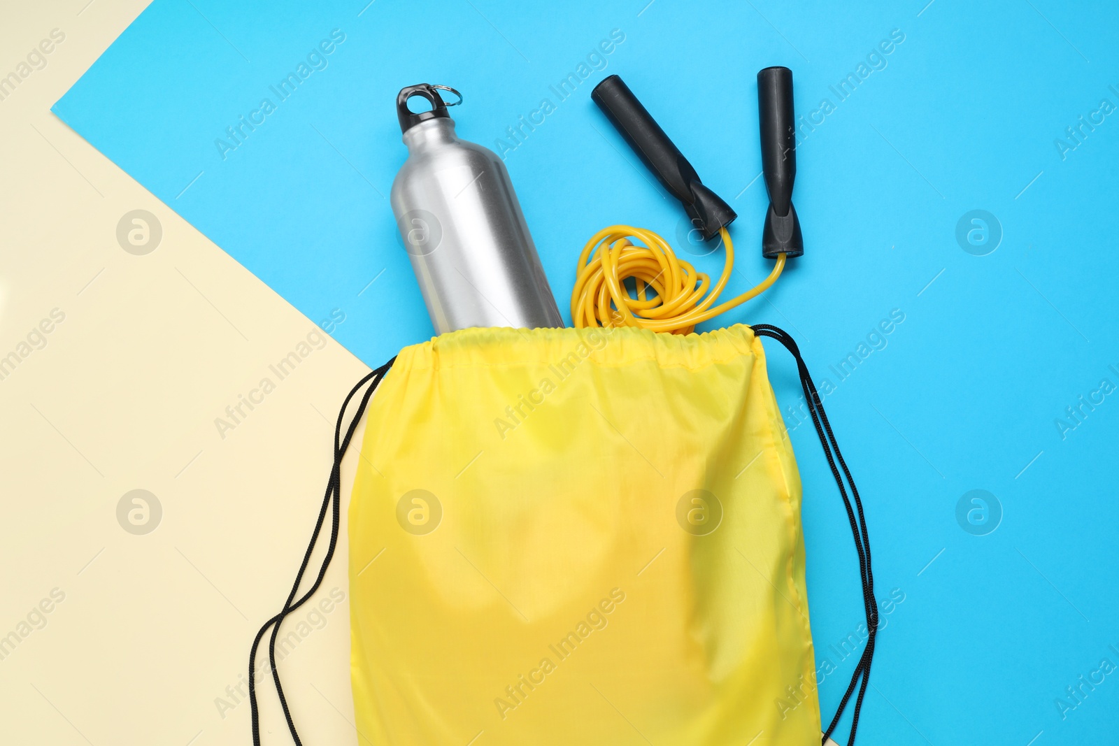 Photo of Yellow drawstring bag, skipping rope and thermo bottle on color background, flat lay