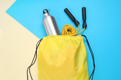 Photo of Yellow drawstring bag, skipping rope and thermo bottle on color background, flat lay