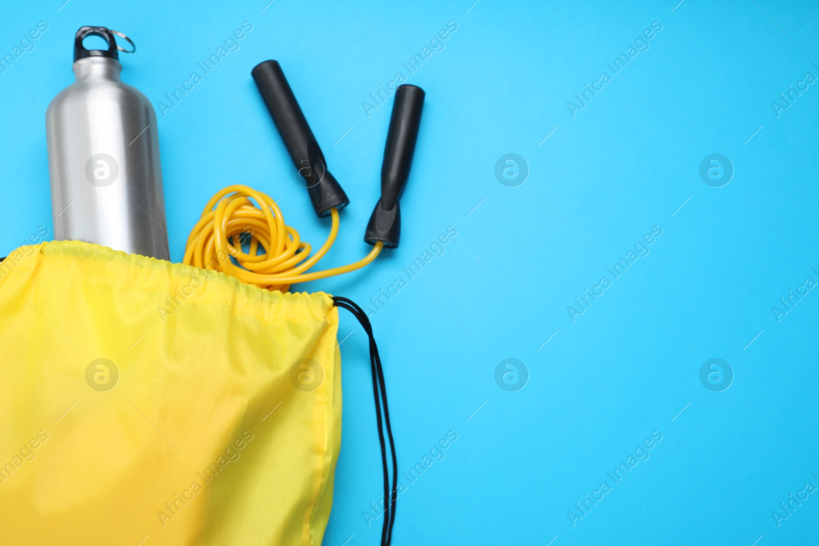 Photo of Yellow drawstring bag, skipping rope and thermo bottle on light blue background, flat lay. Space for text