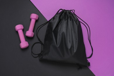 Black drawstring bag and dumbbells on color background, flat lay