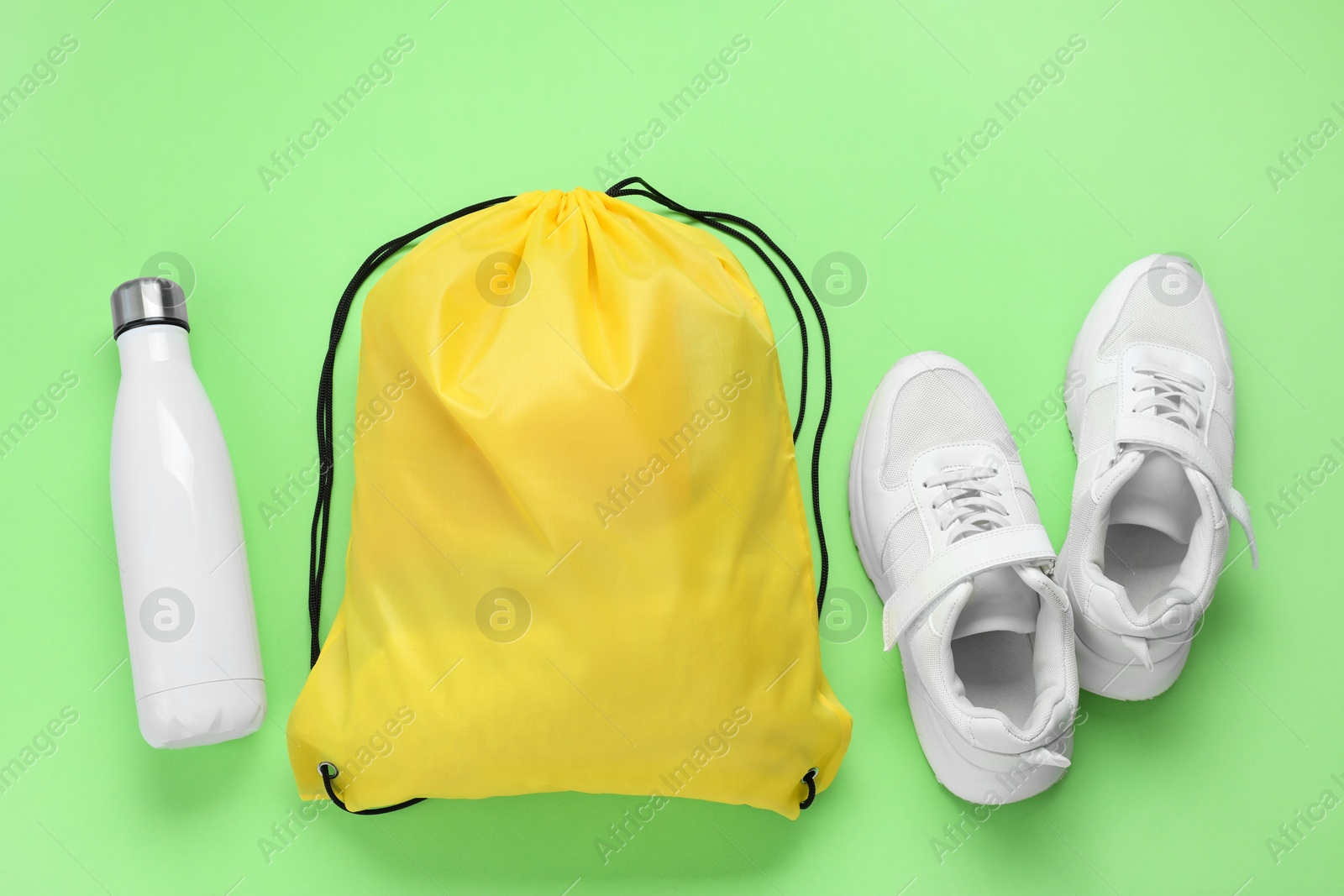 Photo of Yellow drawstring bag, thermo bottle and sneakers on green background, flat lay