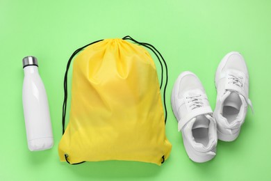 Yellow drawstring bag, thermo bottle and sneakers on green background, flat lay
