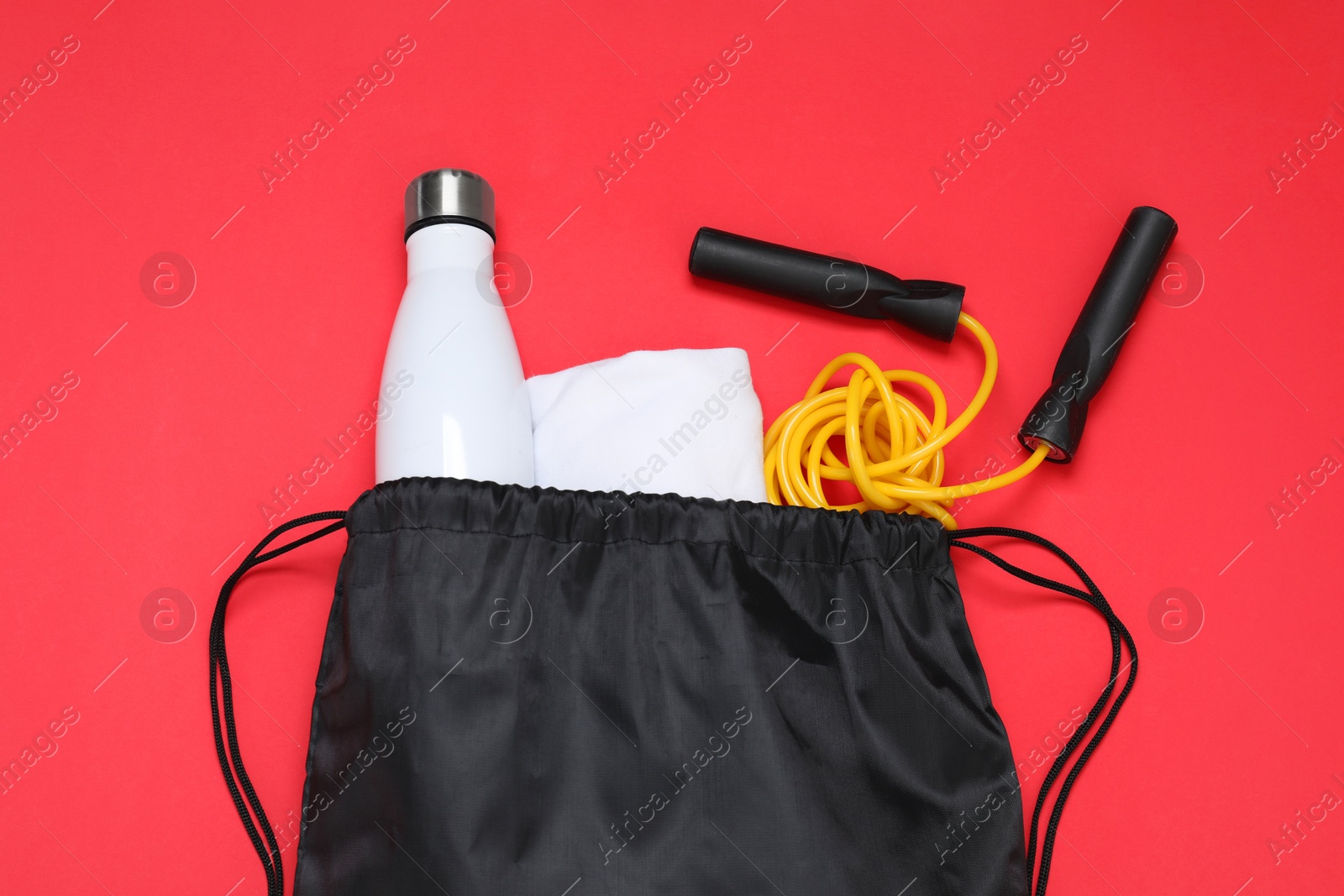 Photo of Black drawstring bag, thermo bottle and skipping rope on red background, flat lay