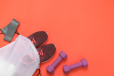 Drawstring bag, sneakers, fitness elastic band and dumbbells on orange background, flat lay. Space for text