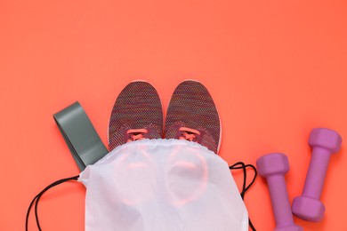 Photo of Drawstring bag, sneakers, fitness elastic band and dumbbells on orange background, flat lay. Space for text