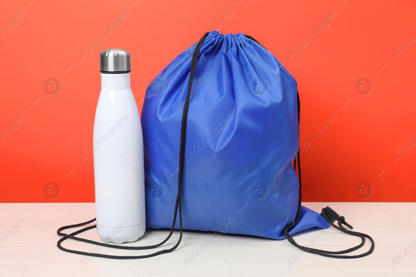 Photo of Blue drawstring bag and thermo bottle on white wooden table