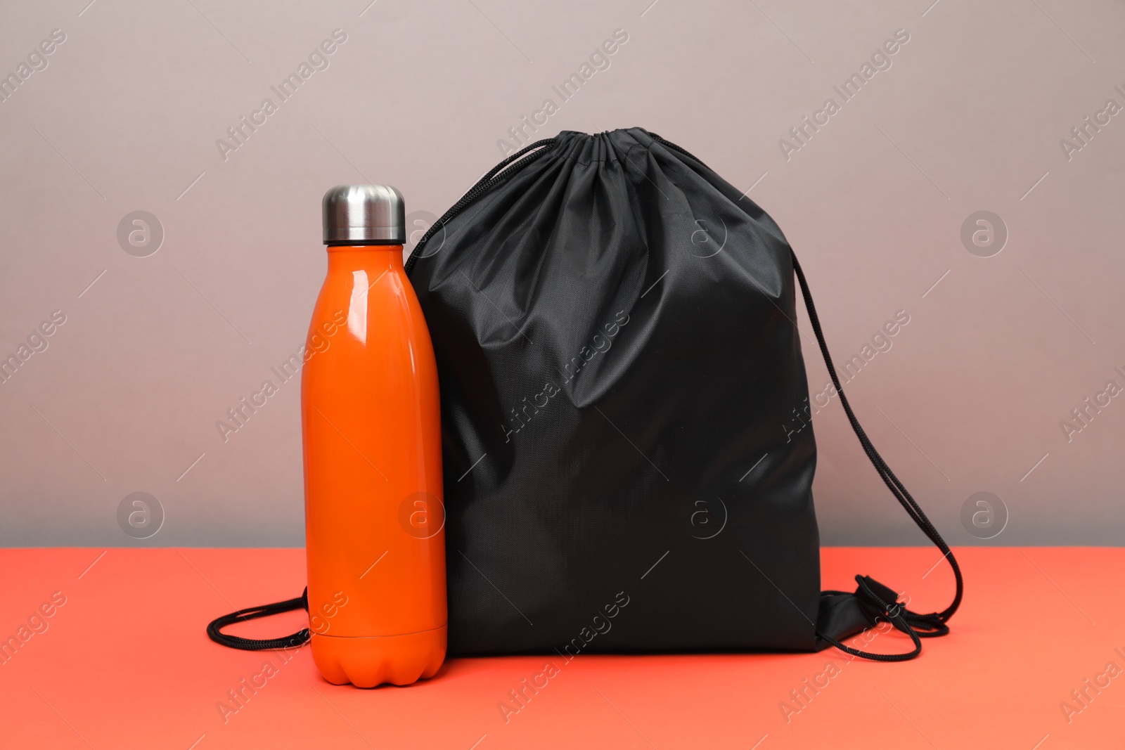 Photo of Black drawstring bag and thermo bottle on grey background