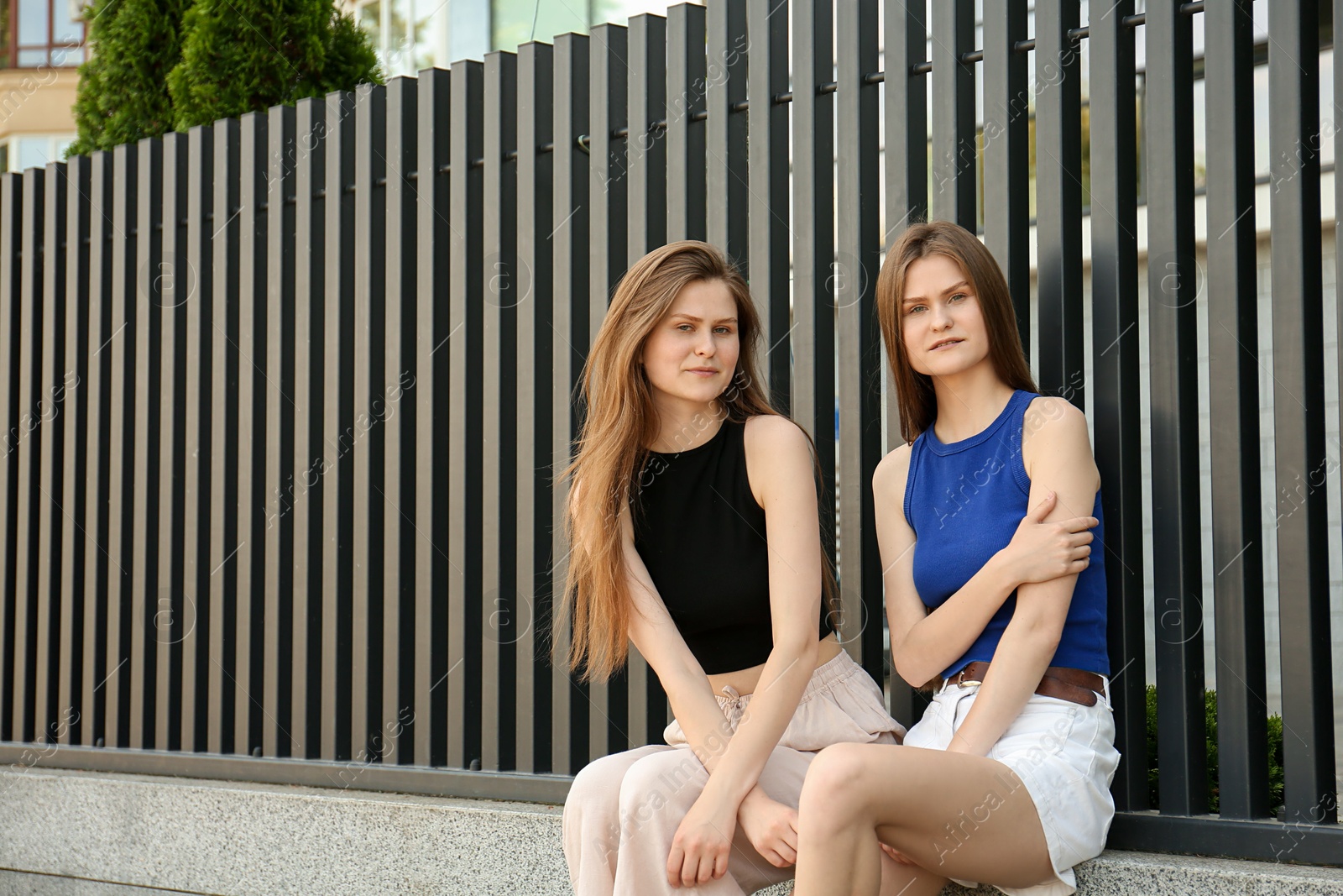 Photo of Two beautiful twin sisters in near metal fence outdoors, space for text