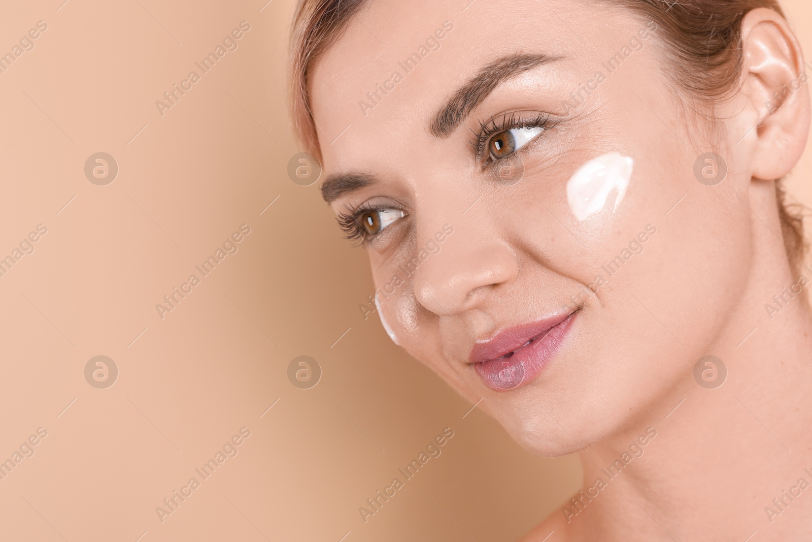 Photo of Beautiful woman with cream on her face against beige background, closeup. Space for text