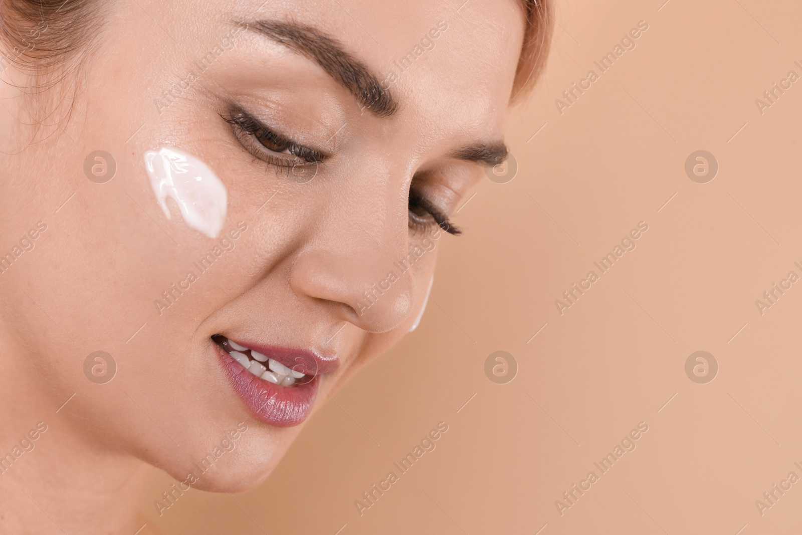 Photo of Beautiful woman with cream on her face against beige background, closeup. Space for text