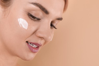 Beautiful woman with cream on her face against beige background, closeup. Space for text