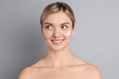 Beautiful woman with cream on her face against gray background