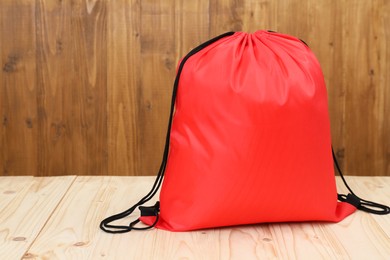 Red drawstring bag on light wooden table. Space for text