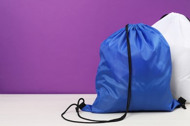 Two drawstring bags on white wooden table against purple background. Space for text