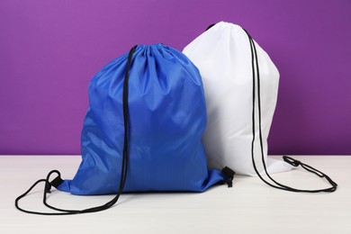 Two drawstring bags on white wooden table against purple background