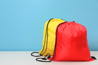 Two drawstring bags on white wooden table against light blue background. Space for text