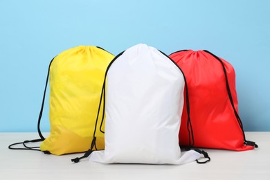 Three drawstring bags on white wooden table against light blue background