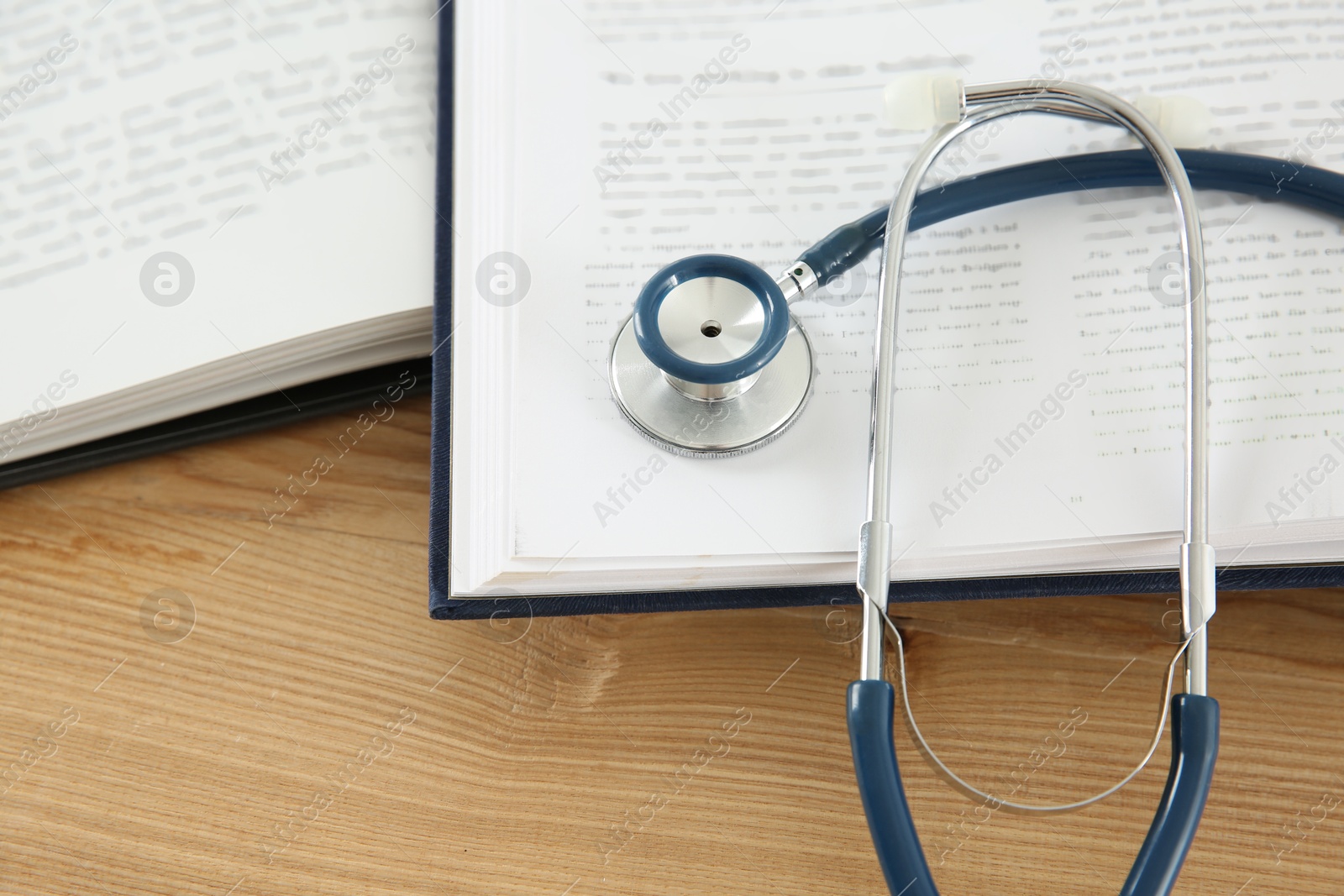 Photo of One new medical stethoscope and books on wooden table, closeup