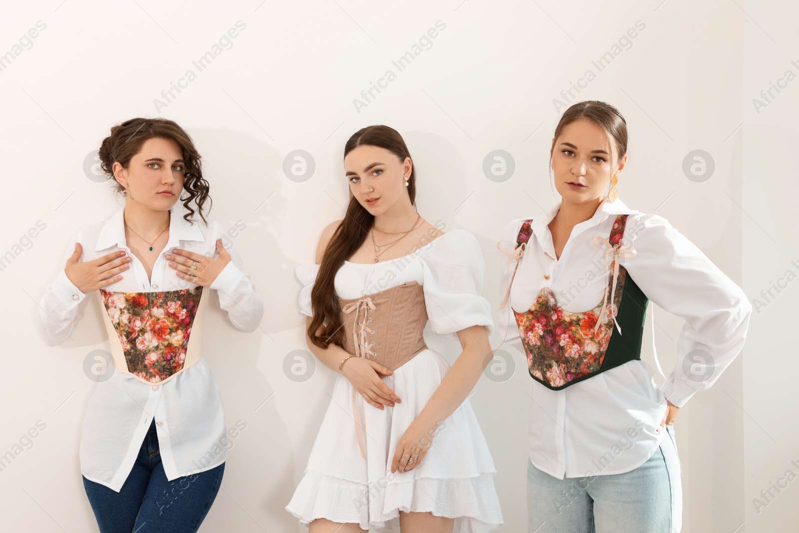 Photo of Beautiful women in stylish corsets posing near light wall