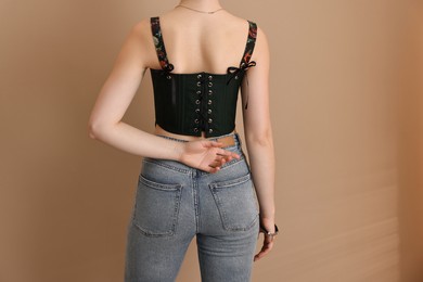 Woman in stylish corset on beige background, back view