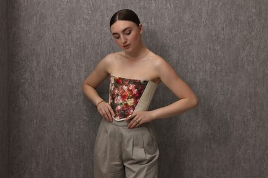 Photo of Beautiful young woman in stylish corset near grey wall