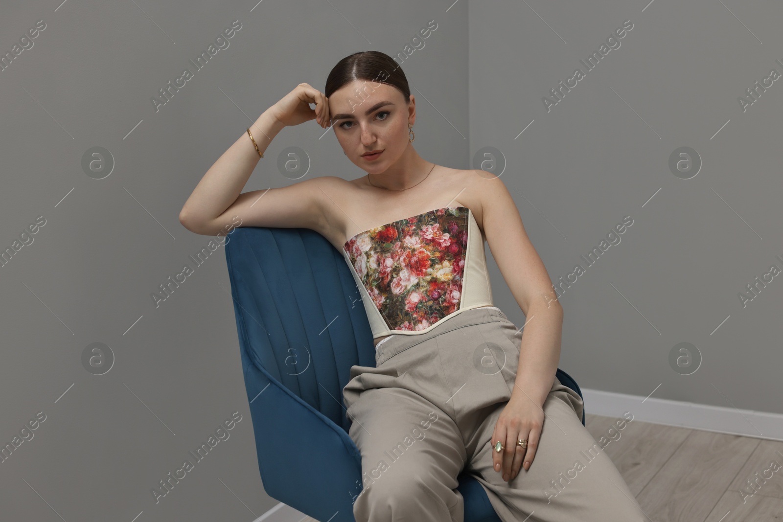Photo of Beautiful young woman in stylish corset on armchair indoors