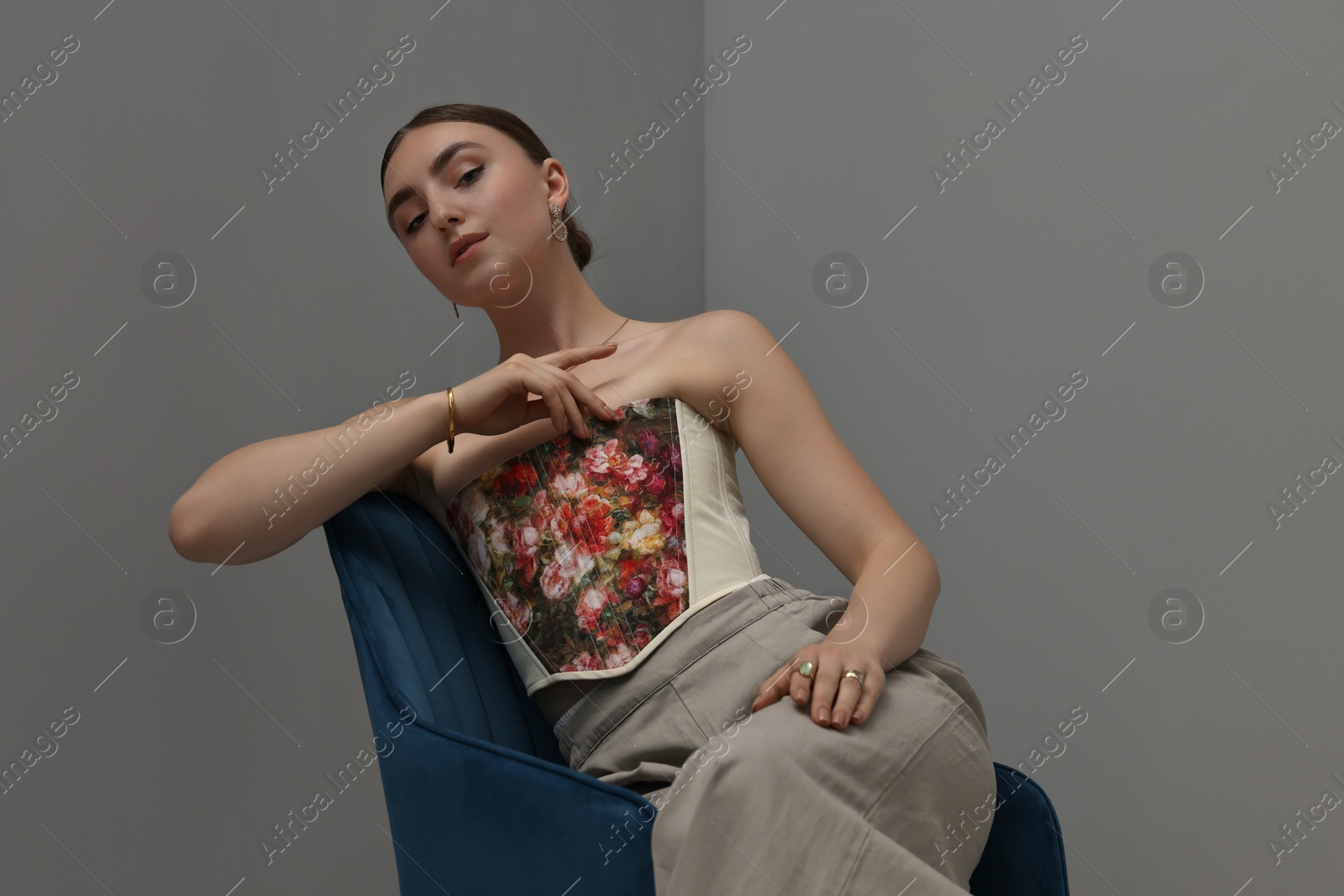 Photo of Beautiful young woman in stylish corset on armchair indoors