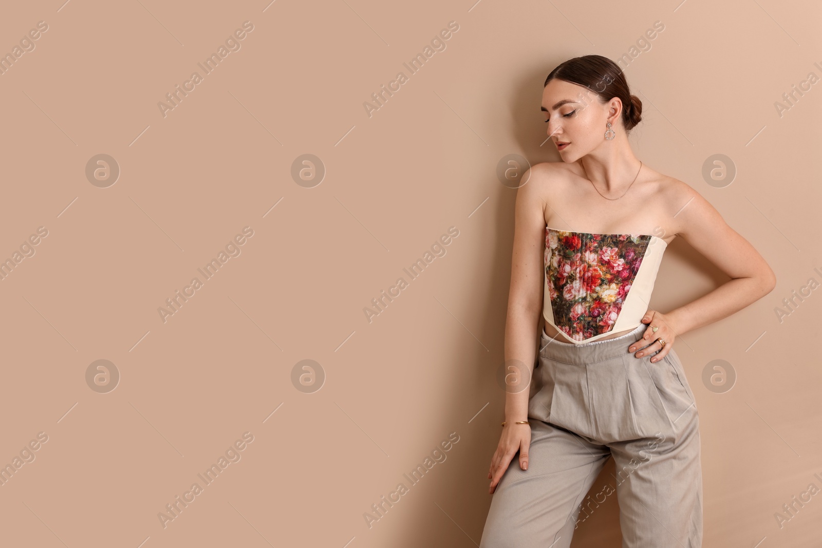 Photo of Beautiful young woman in stylish corset near beige wall, space for text