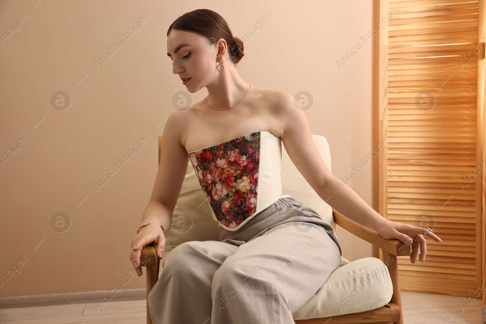 Photo of Beautiful young woman in stylish corset on armchair indoors