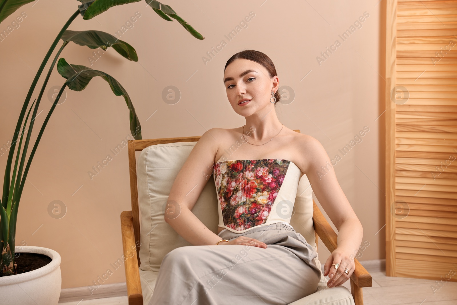 Photo of Beautiful young woman in stylish corset on armchair indoors