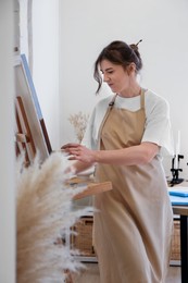 Photo of Woman drawing on easel with canvas in studio