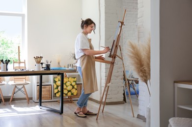 Photo of Woman drawing on easel with canvas in studio