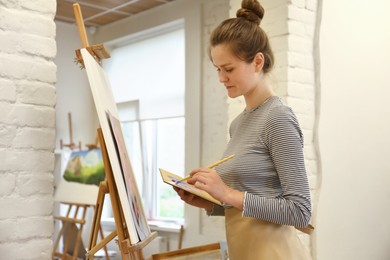 Photo of Woman drawing on easel with canvas in studio