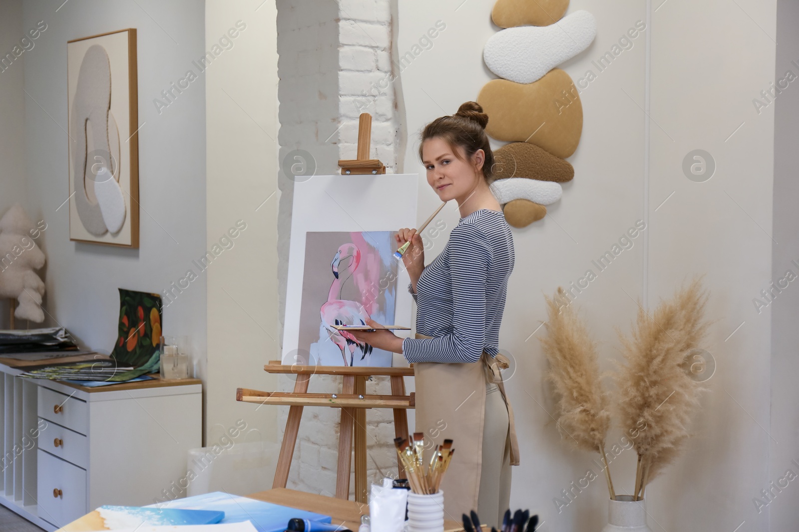 Photo of Portrait of woman with brush and palette near her artwork in drawing studio