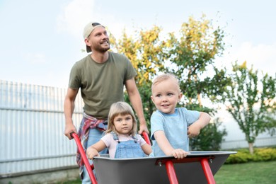 Photo of Father pushing wheelbarrow with his kids outdoors