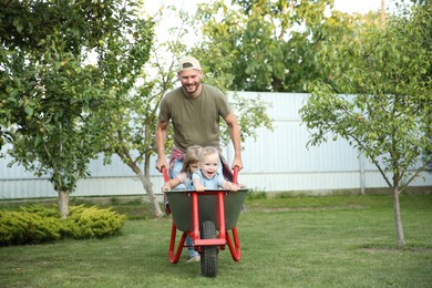 Father pushing wheelbarrow with his kids outdoors