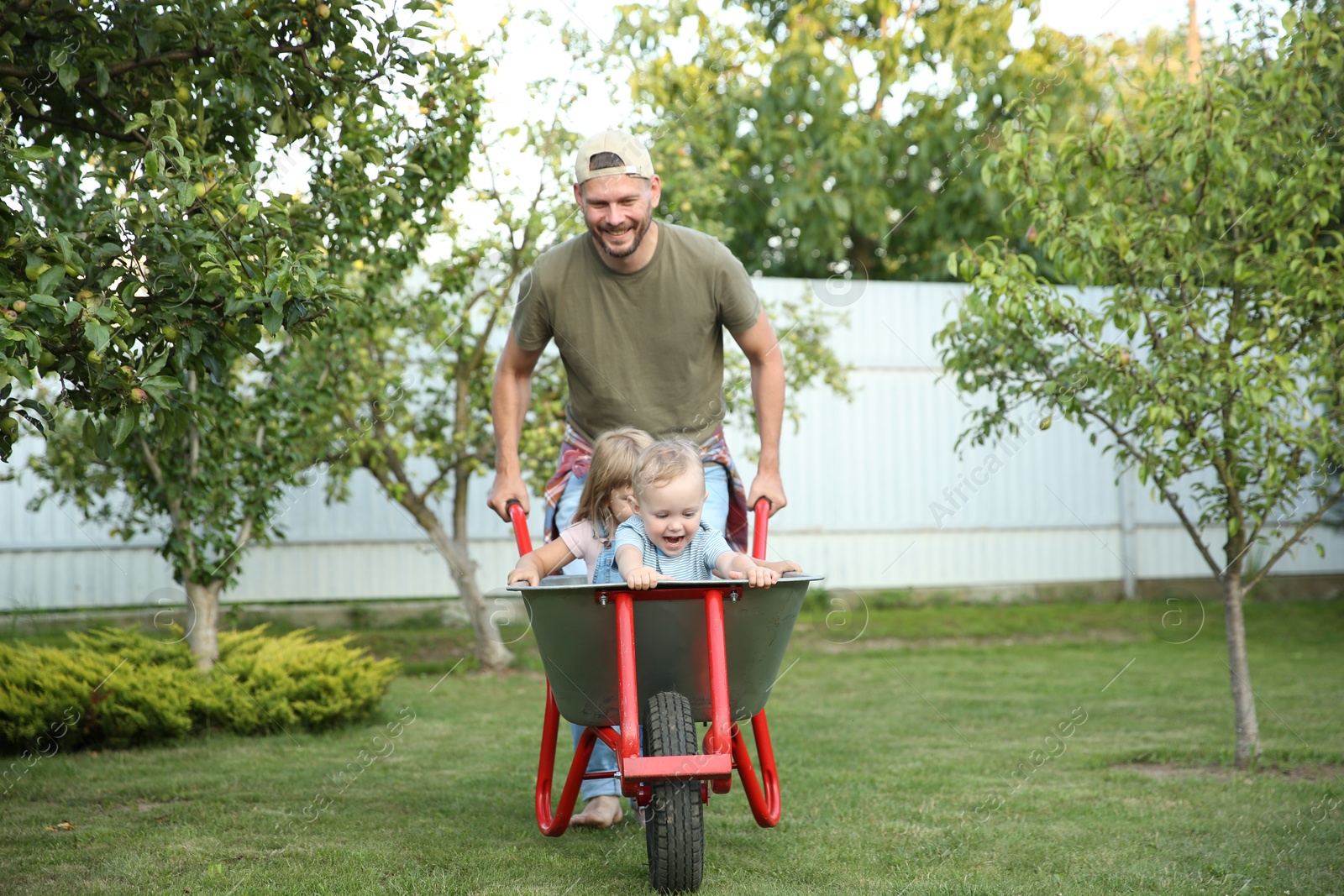 Photo of Father pushing wheelbarrow with his kids outdoors